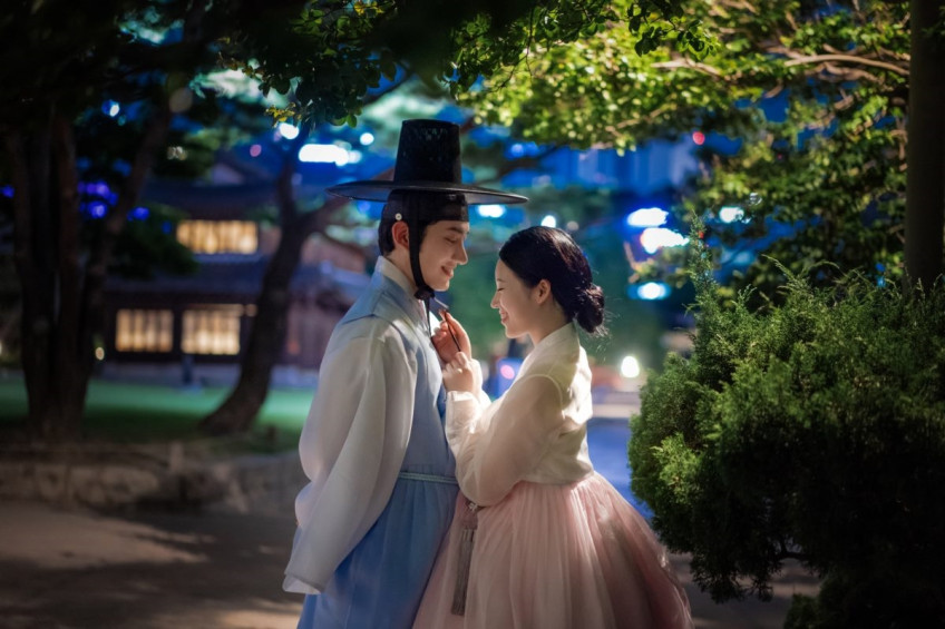 나뭇잎과 푸른 밤빛 아래, 한복을 입은 두 사람이 가까이 마주 서서 서로를 바라본다